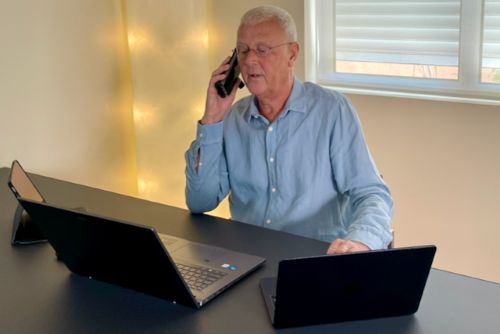 Foto van Roel van Arise aan zijn werkplek, aan de telefoon met laptop en tablet op het bureau
